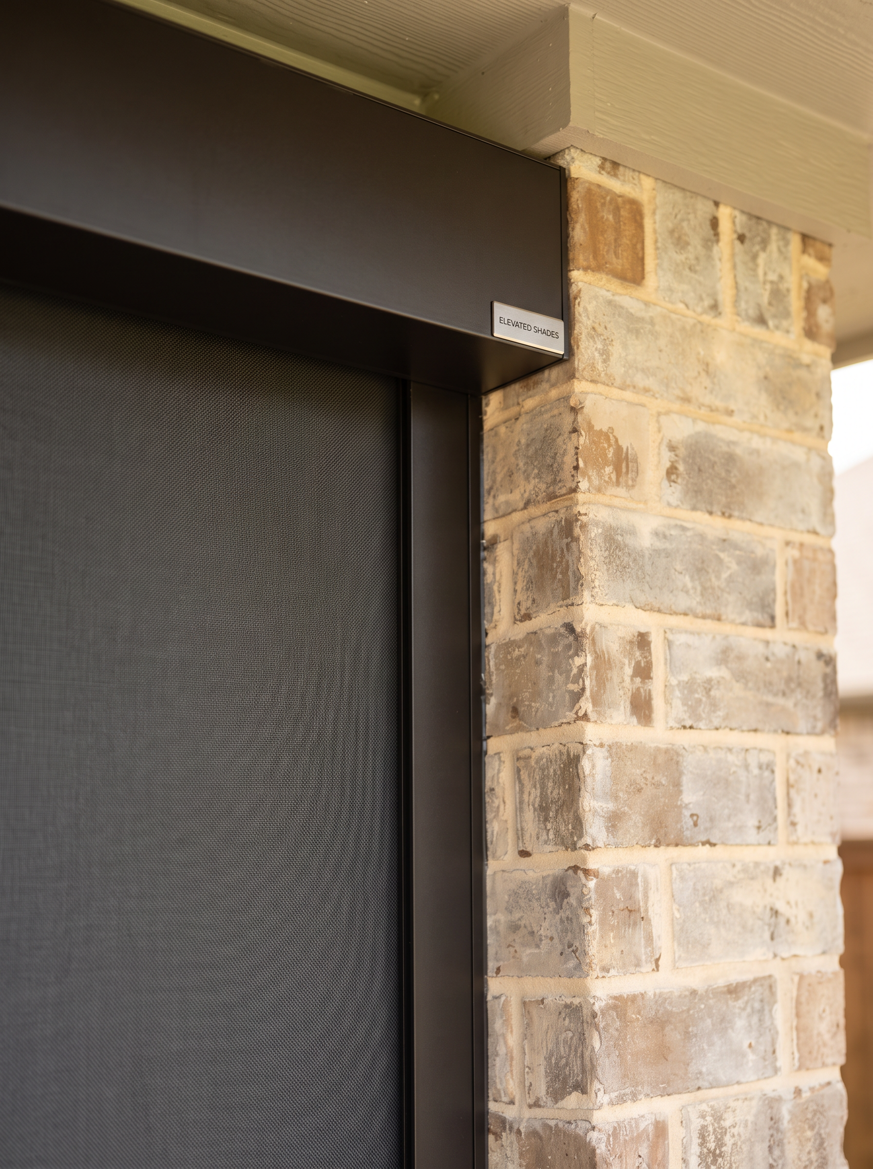 Dark bronze motorized shade cassette and zip-track channel installed against brick